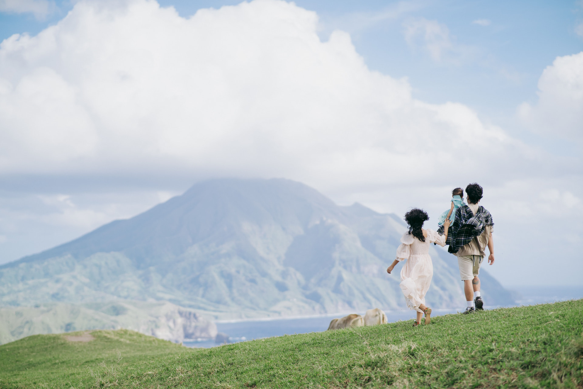 A family walking a grassy ridge with a mountain and coastline beyond