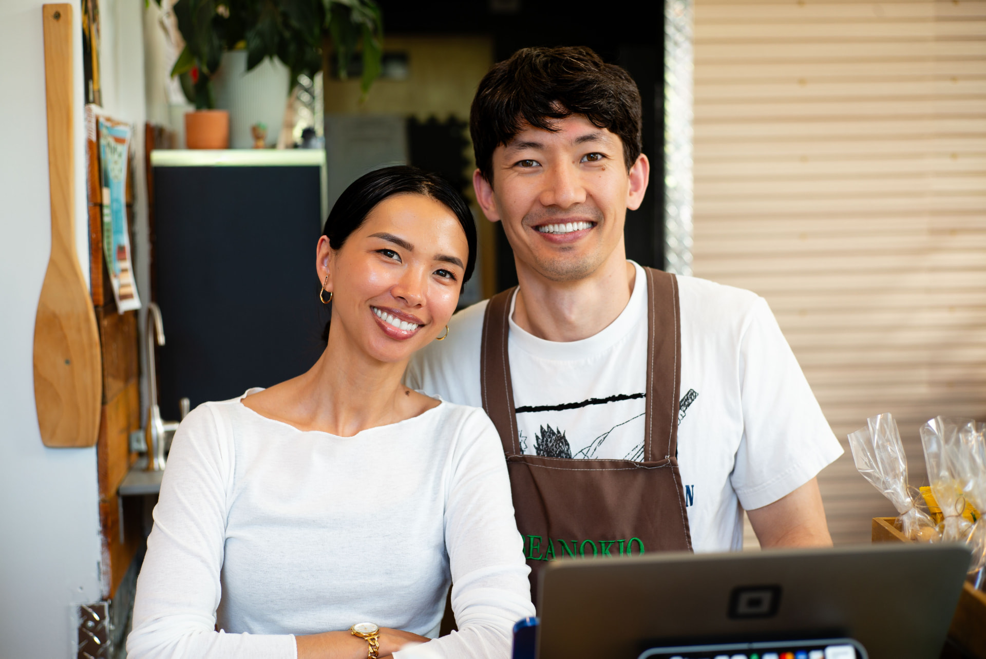 Two small-business owners smiling behind the counter of their shop