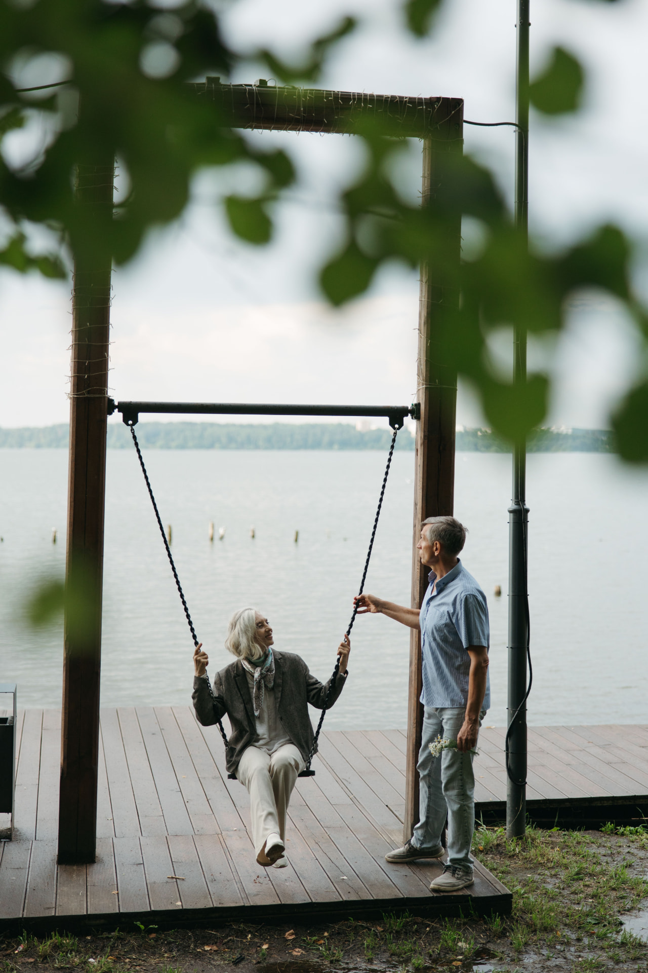 An older couple by the lake, one on a swing, at the end of a workday